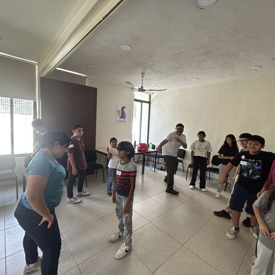 Niñas y niños formados en círculo durante una dinámica dentro del salón