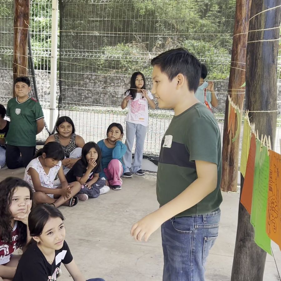 Niño presentando su historia frente al grupo, con hojas de colores colgadas