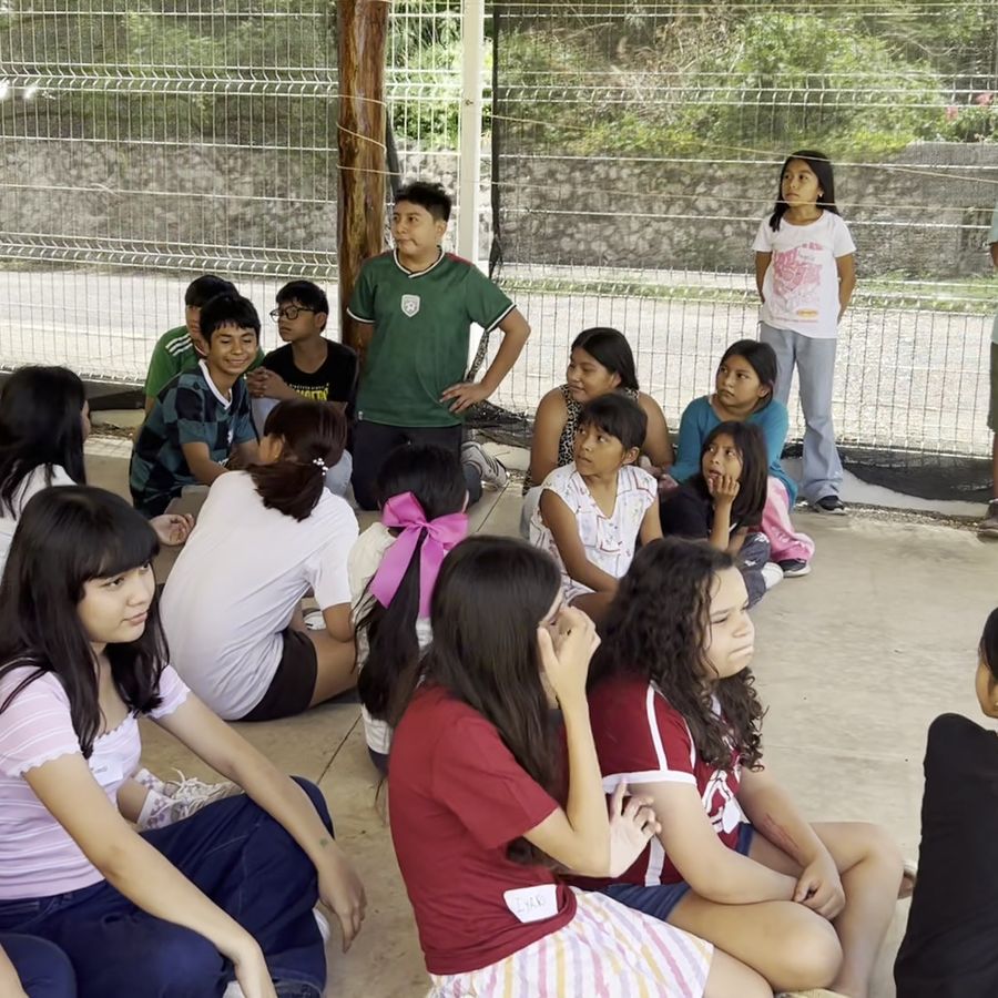 Grupo de niñas y niños sentados en círculo al aire libre durante una dinámica